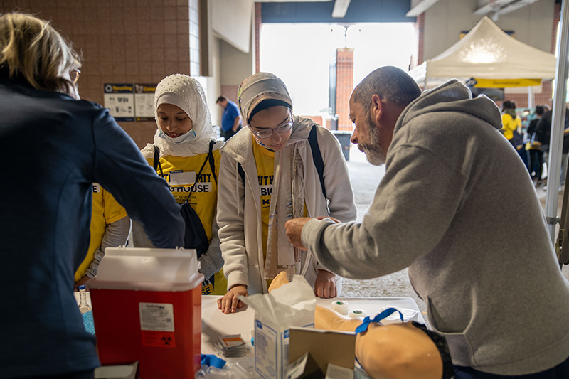 Juan Torres explaining phlebotomy with a fake arm on the table.